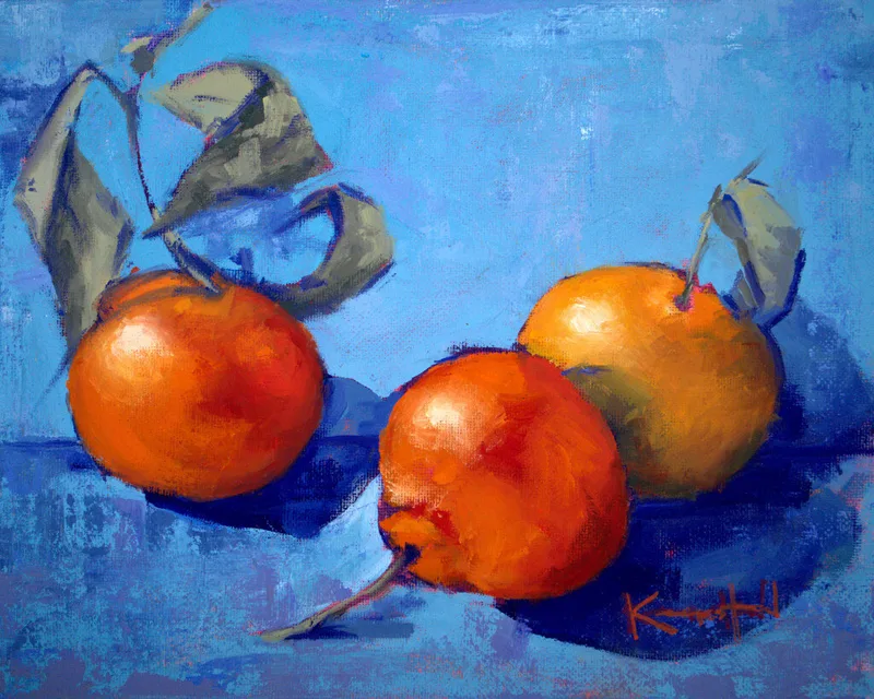 still life of three orange tangerines with leaves on a blue tabletop