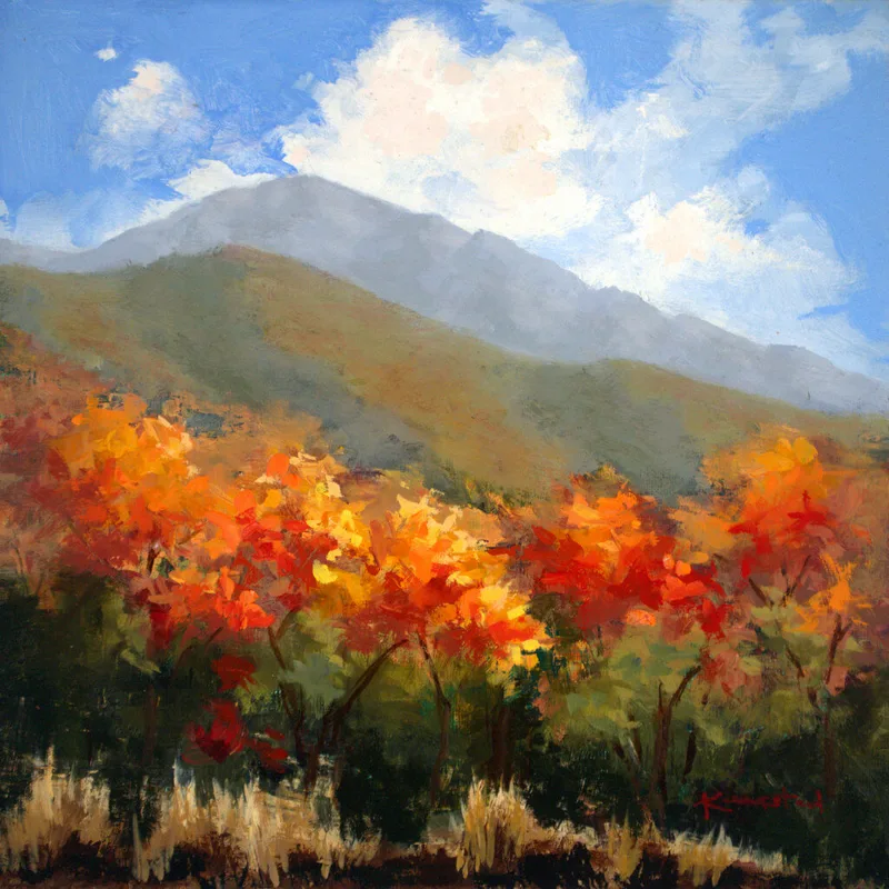 landscape with vibrant orange autumn trees beneath gray mountain and clouded sky