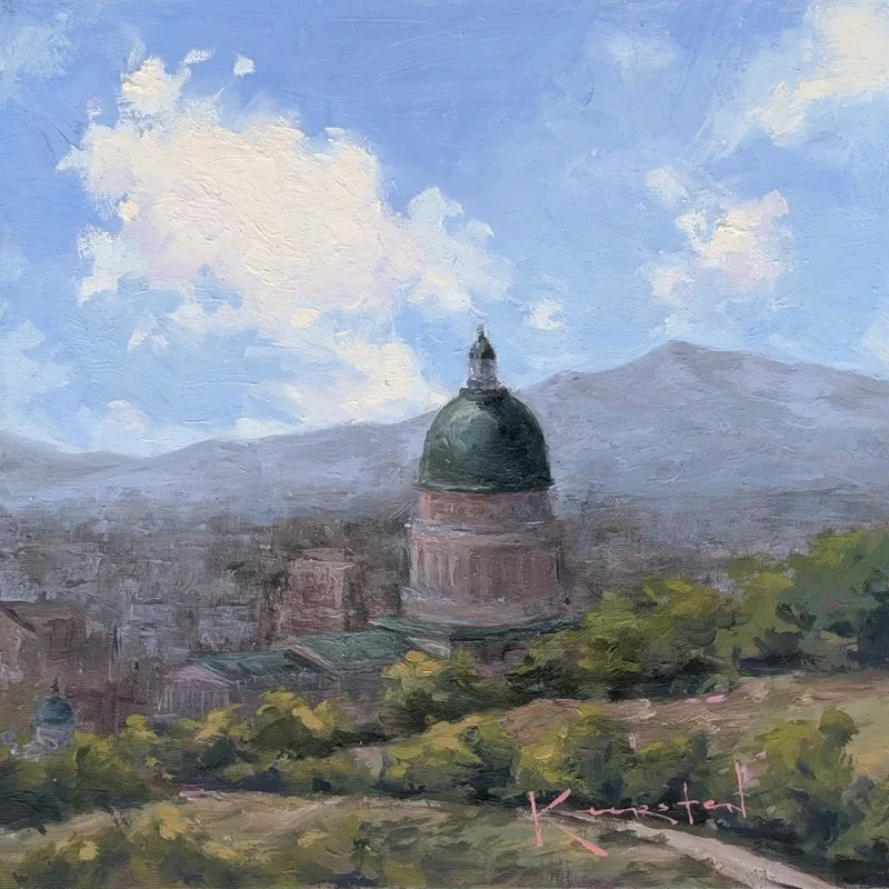 Green-domed capitol rising above city trees, with clouds and mountains beyond.