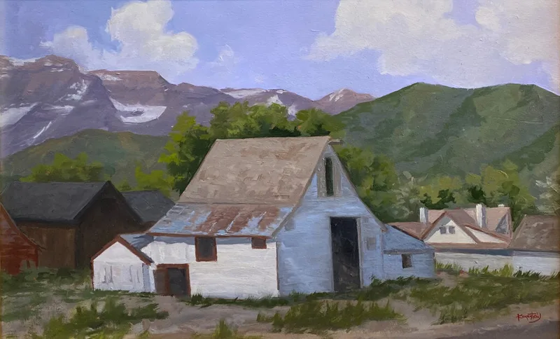 White barn and outbuildings nestled below rugged snow-streaked mountain peaks and green hills