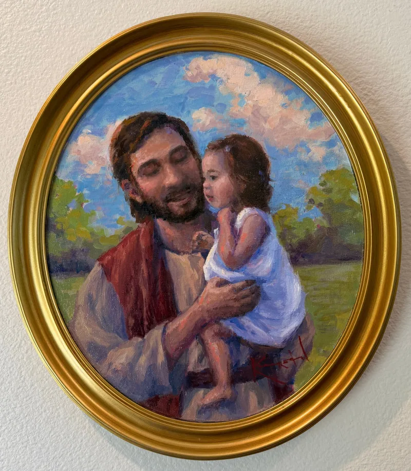 Christ in red and cream robes holding a small child in a white dress, summer landscape behind, oval gold frame.