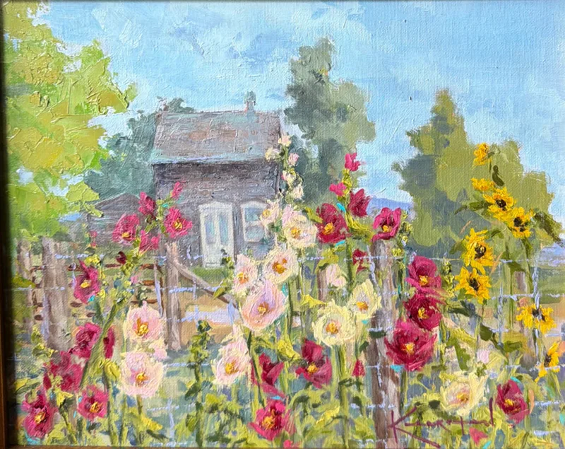 Sunflowers and hollyhocks blooming in front of a cottage with a covered porch.