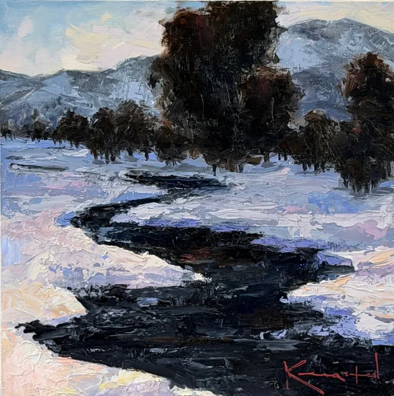 Dark winding stream cutting through snowy banks with bare trees and distant mountains