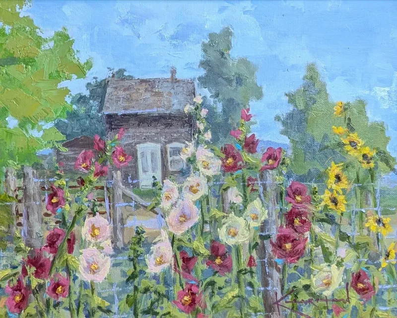 Pink and red hollyhocks with sunflowers along a fence before a small weathered cottage.