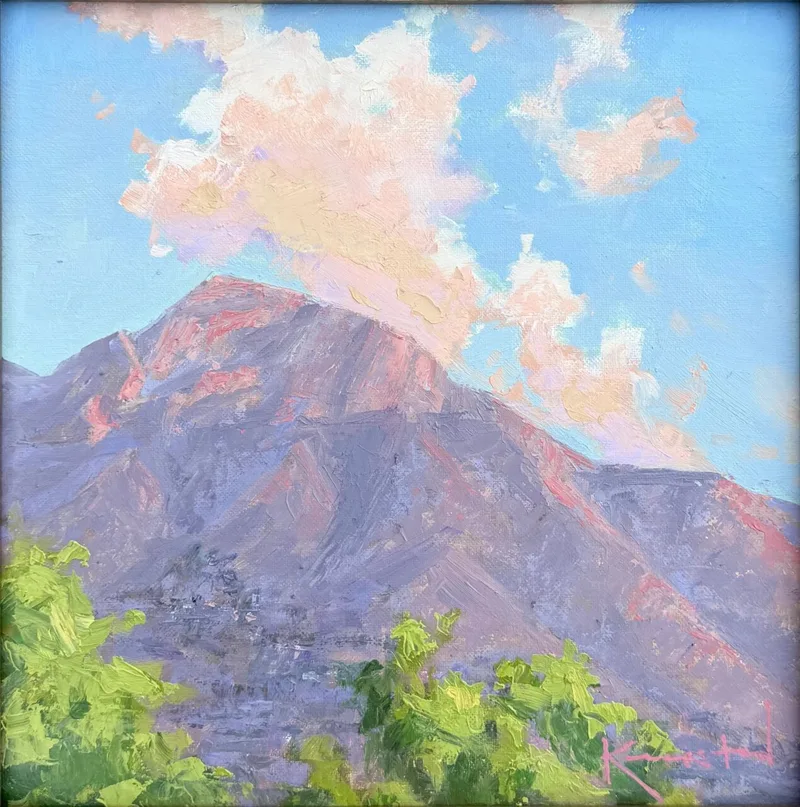 Purple desert mountain peak with pink-tinged clouds above and green foliage below
