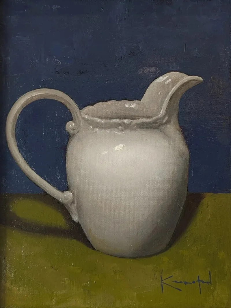White ceramic pitcher with curved handle on green surface against deep blue