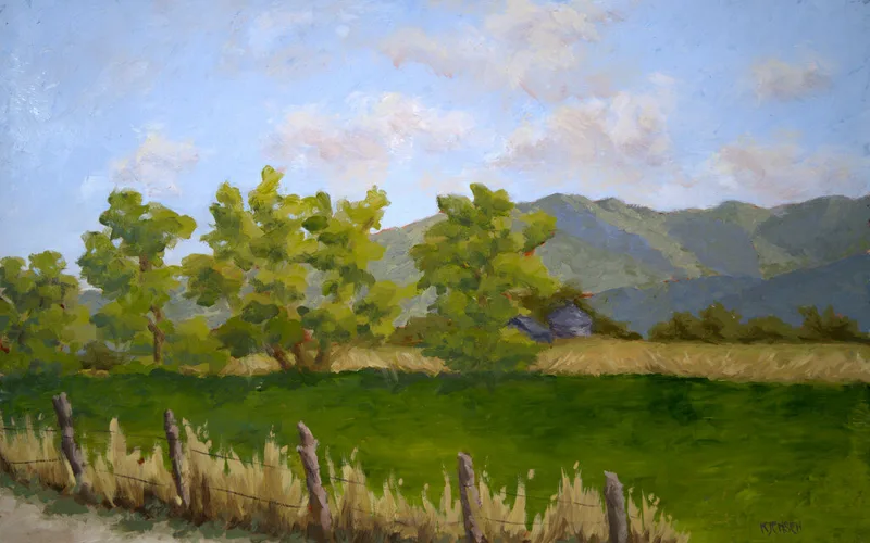 Wire fence along grassy field with leafy trees and distant blue mountains
