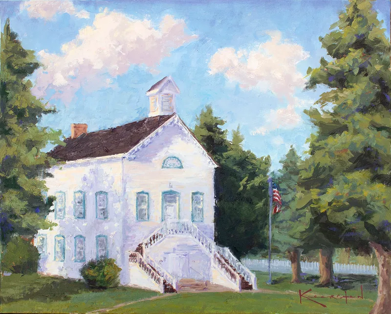 Historic white Pine Valley chapel with a small steeple, framed by tall green pines, a white picket fence, and an American flag under a blue summer sky.