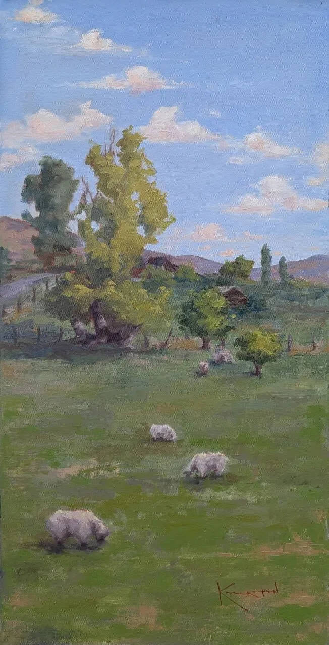 Sheep grazing in a green pasture with tall trees and distant hills beneath cloudy sky.