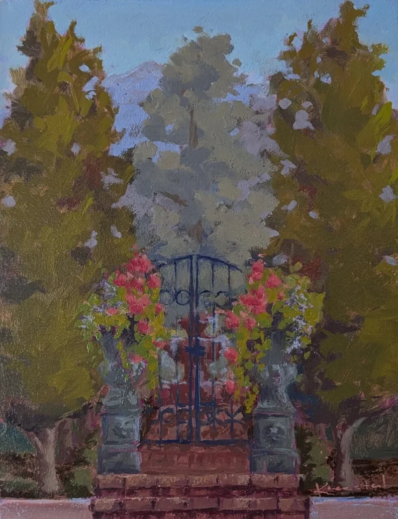Iron garden gate flanked by trees and pink flowers under hazy sky