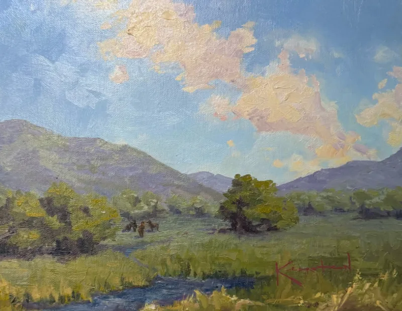 Green valley pastures with a winding stream, scattered trees, and clouds over distant blue mountains.