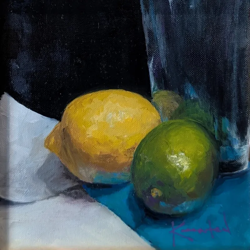 A yellow lemon and green lime beside a dark glass vessel on teal cloth.