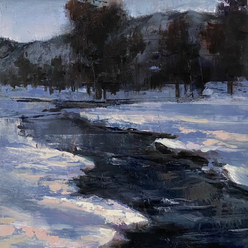 Dark river water flowing past snowy banks with bare trees on distant hillside